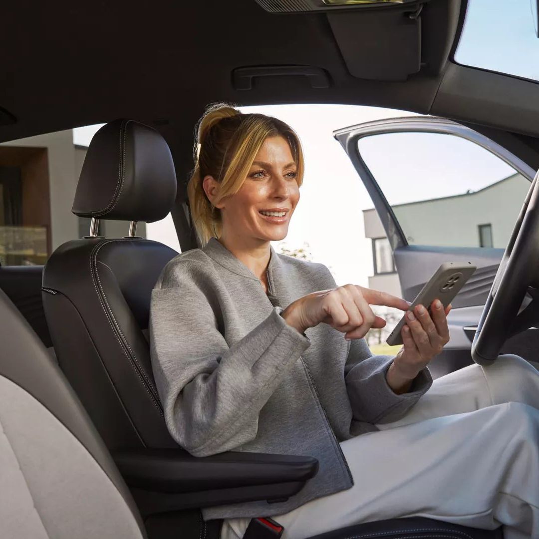 Žena sedí vo vozidle Volkswagen a ťuká na mobilný telefón.