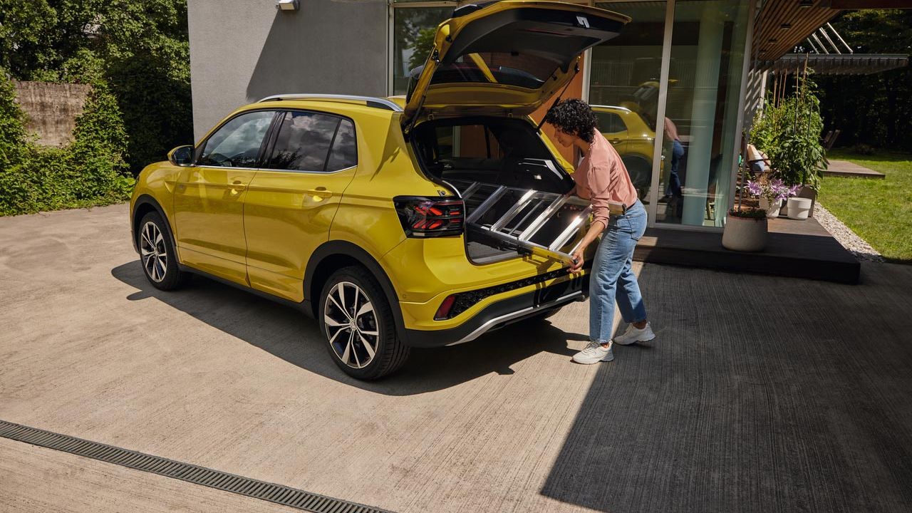 Mladá žena vkladá rebrík do kufra žltého VW T-Cross.