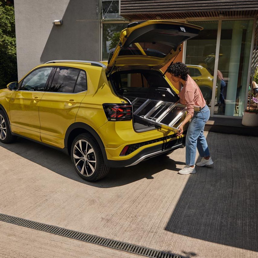 Mladá žena vkladá rebrík do kufra žltého VW T-Cross.