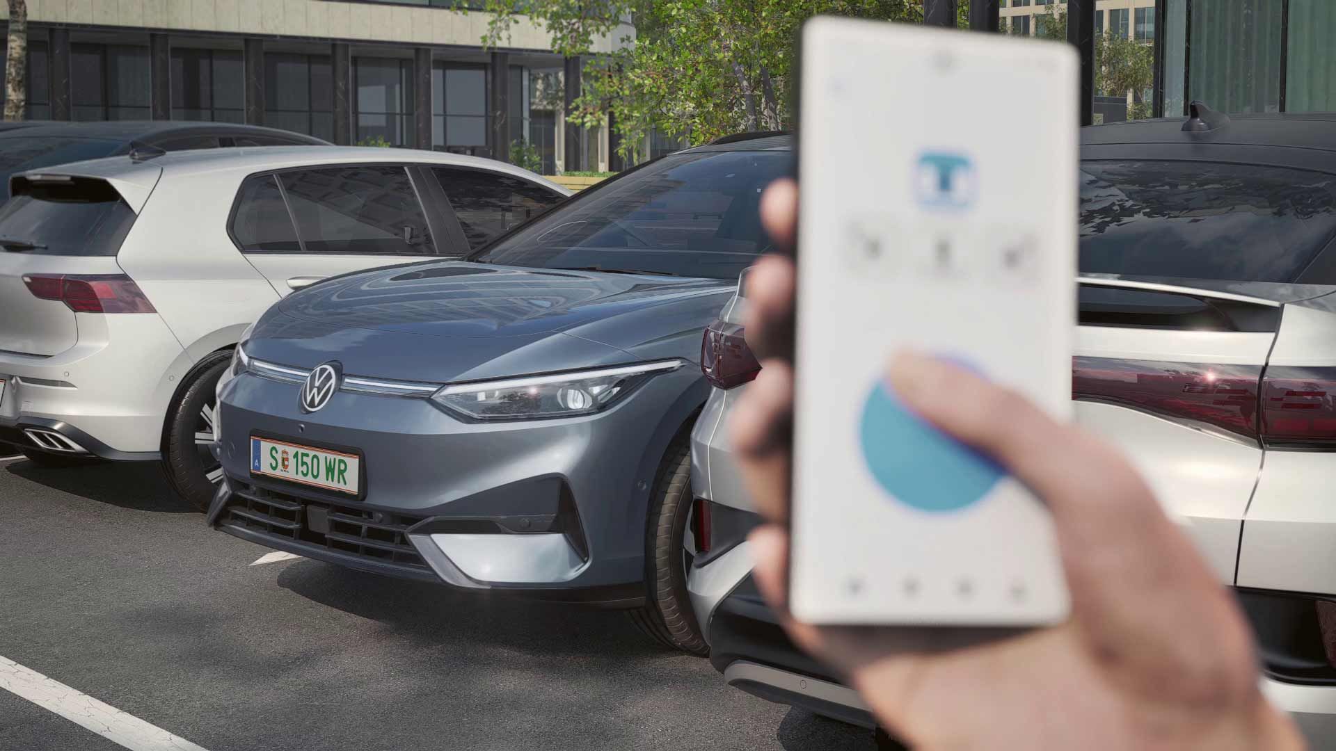 Jedna osoba drží v ruke smartfón a pomocou neho ovláda sivé elektrické auto značky Volkswagen, ktoré je zaparkované medzi dvoma ďalšími autami. Zdá sa, že auto práve vychádza z parkoviska. V pozadí sú vidieť moderné budovy.