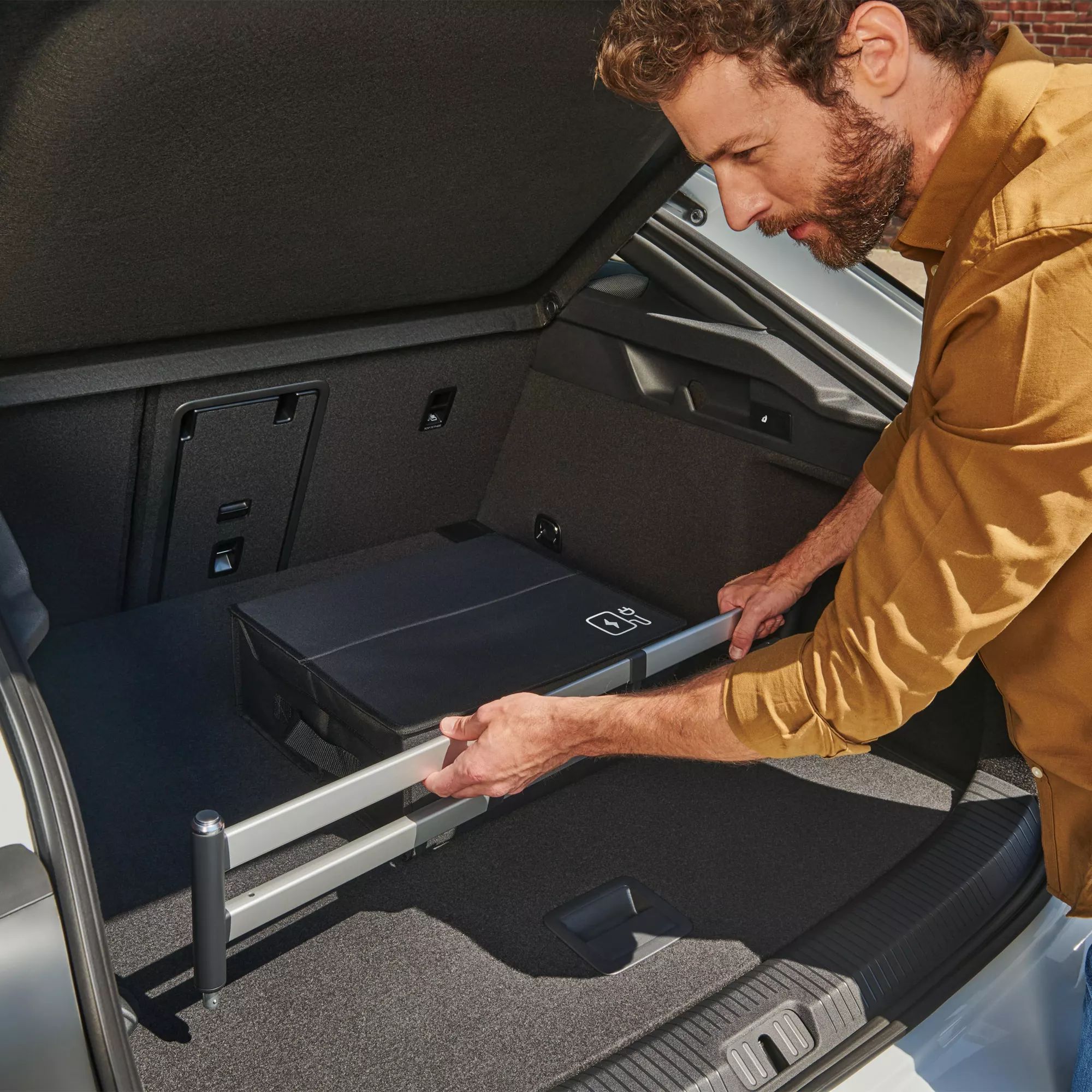 Muž upevňuje zásuvný modul do batožinového priestoru od príslušenstva VW v batožinovom priestore vozidla VW ID.7