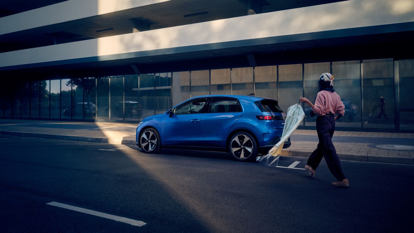 Modrý VW ID. Polo Style stojí zaparkovaný bokom pri okraji cesty, k vozidlu kráča žena.