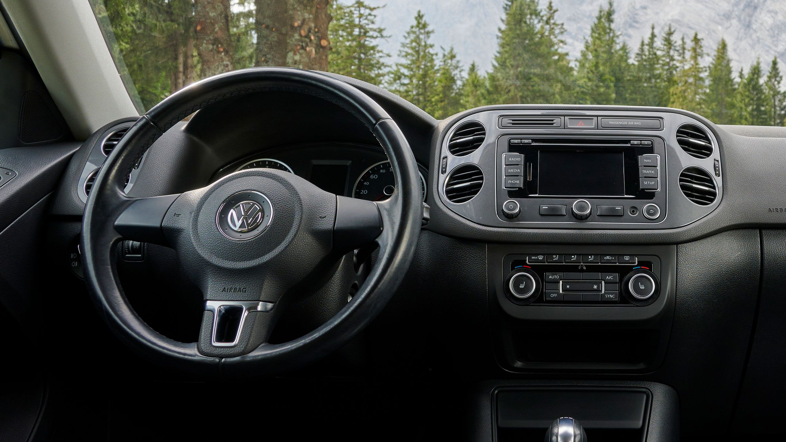 Interiér vozidla VW so zameraním na volant a palubnú dosku – pohľad z vozidla s lesom na pozadí