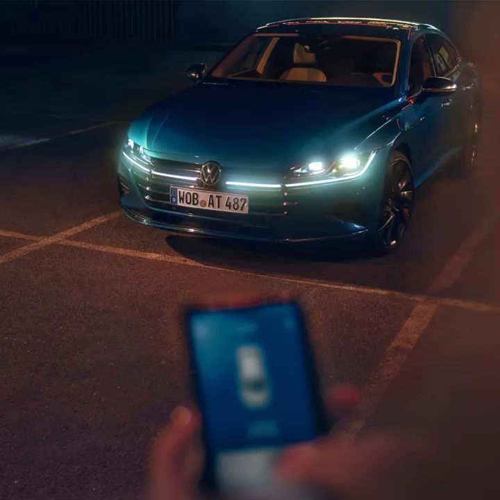Osoba stojí pred vozidlom Volkswagen a drží smartfón v ruke. Na displeji je zobrazená aplikácia Volkswagen.