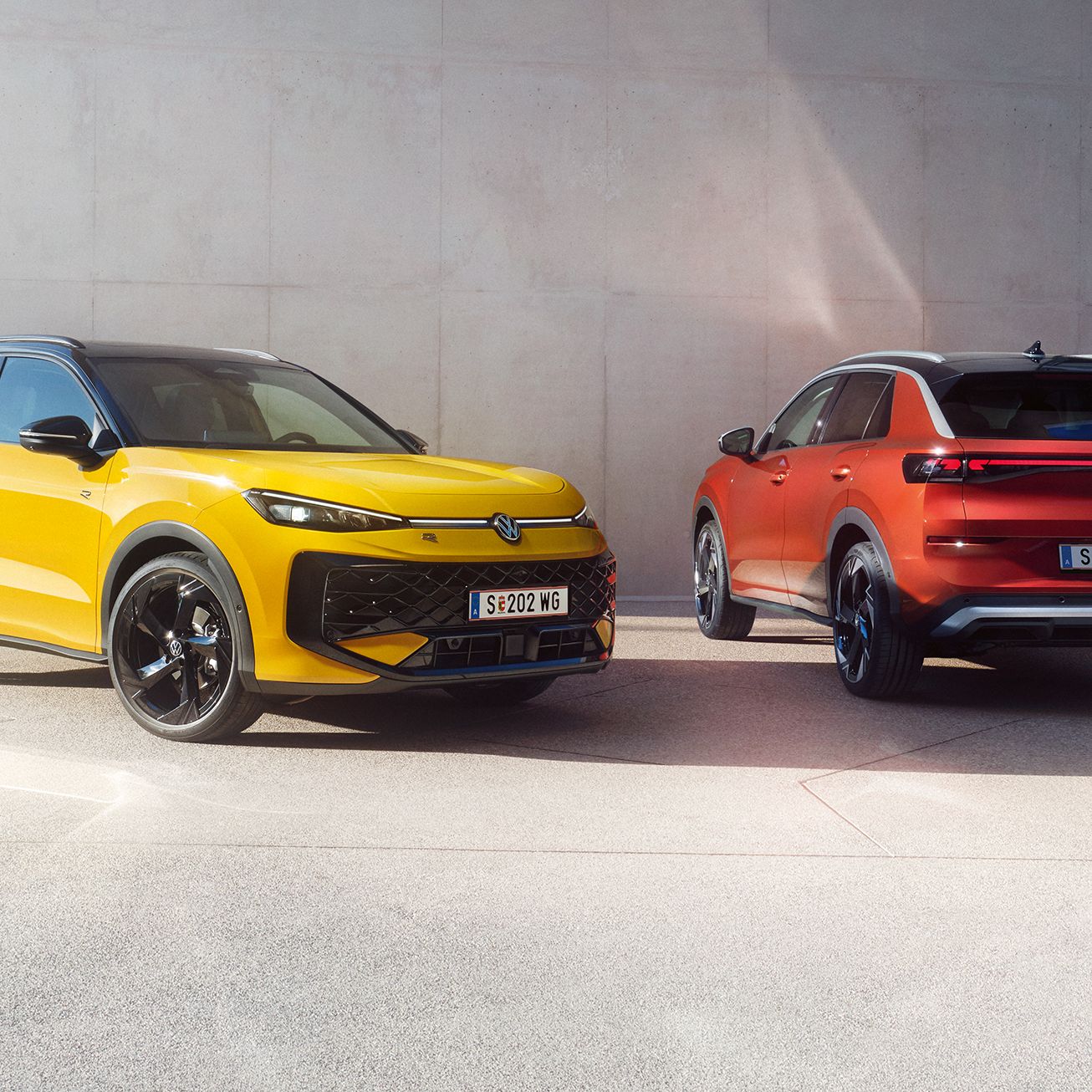 Žltý VW T-Roc R-Line a červený VW T-Roc Style stoja vedľa seba pred modernou budovou.
