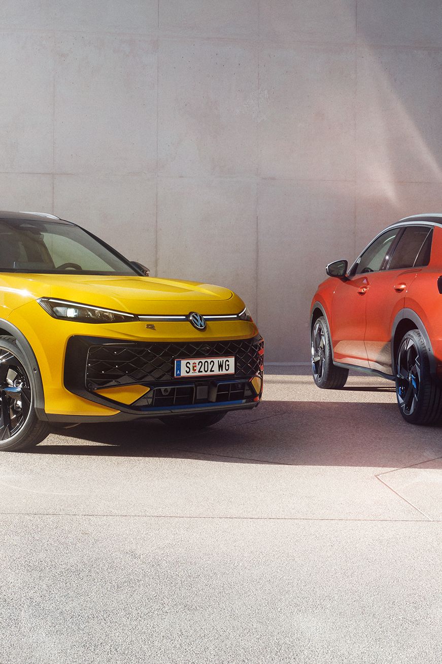 Žltý VW T-Roc R-Line a červený VW T-Roc Style stoja vedľa seba pred modernou budovou.
