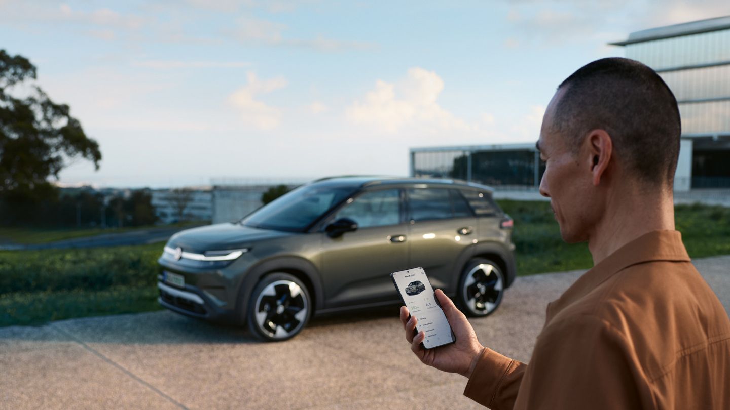 Zelený VW ID.Cross stojí pri obytnom dome, vedľa neho stojí muž, ktorý sa pozerá do svojho smartfónu.