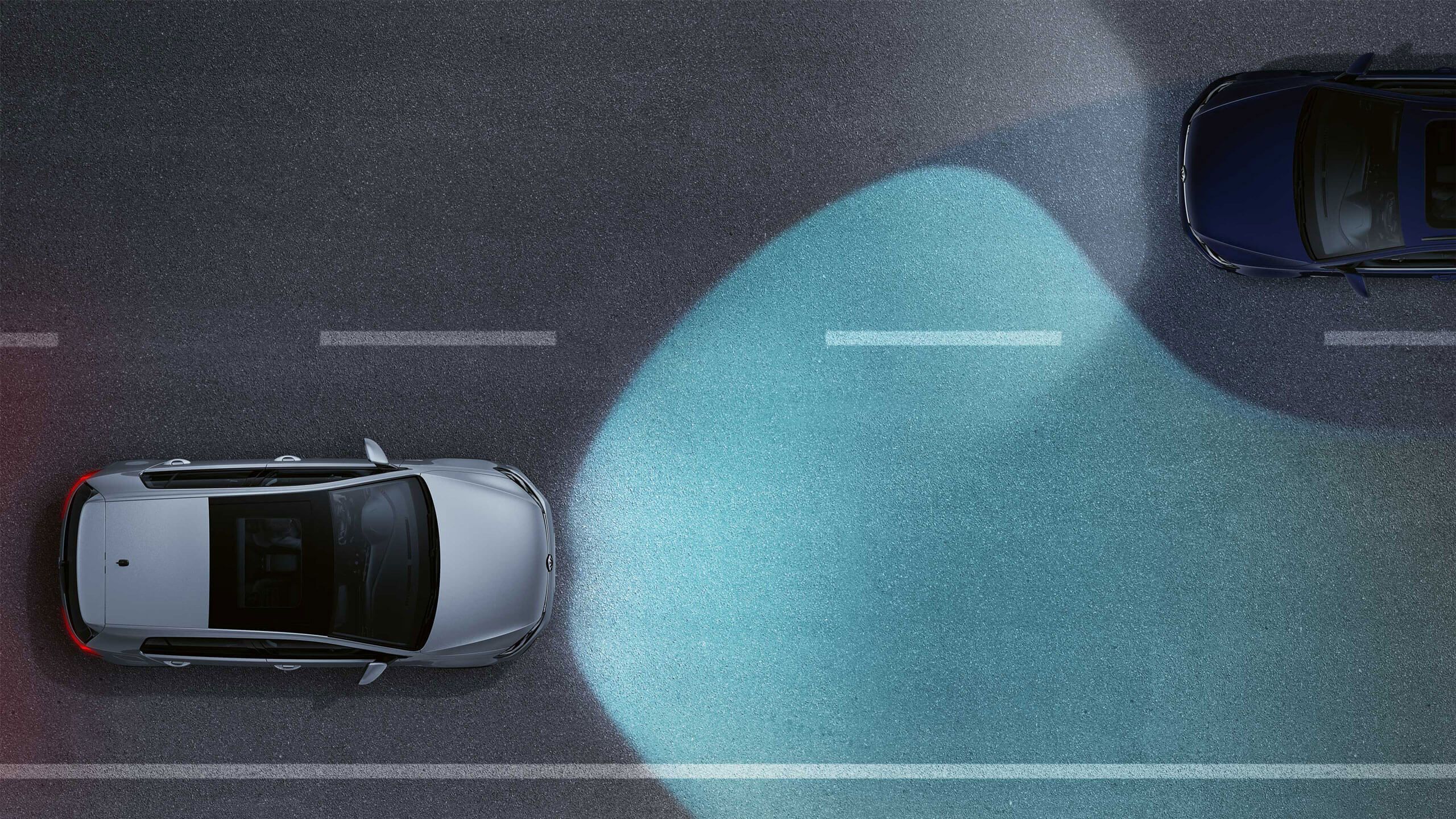 Automobil na ceste so zapnutými adaptívnymi diaľkovými svetlami s odtieneným osvetlením vozidiel v protismere. Oproti ide po ceste ďalší automobil so zapnutými stretávacími svetlami. Cesta má vyznačené jazdné pruhy.