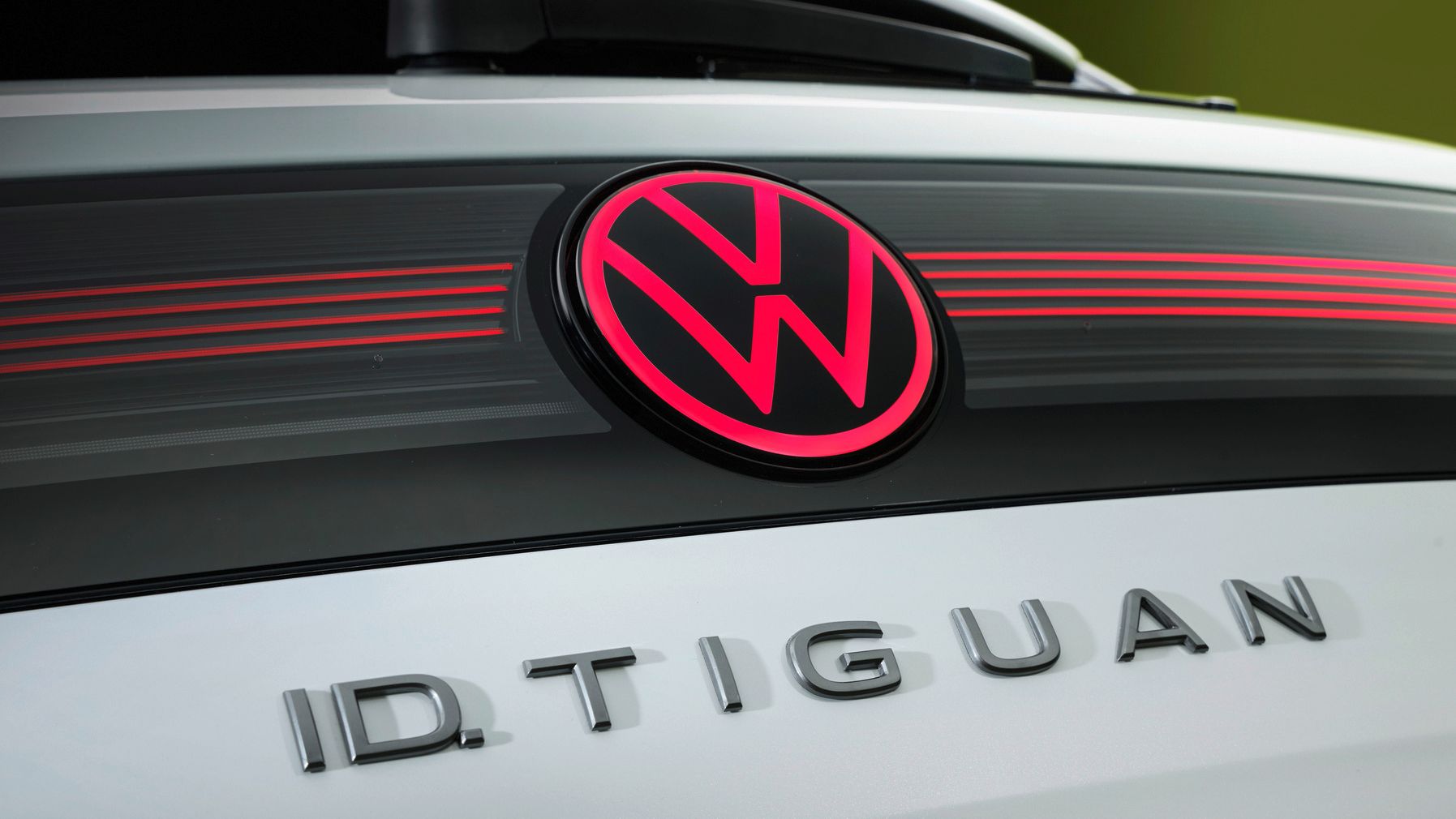 Detailný pohľad na osvetlené logo VW a názov modelu ID. Tiguan na zadných dverách bieleho vozidla.