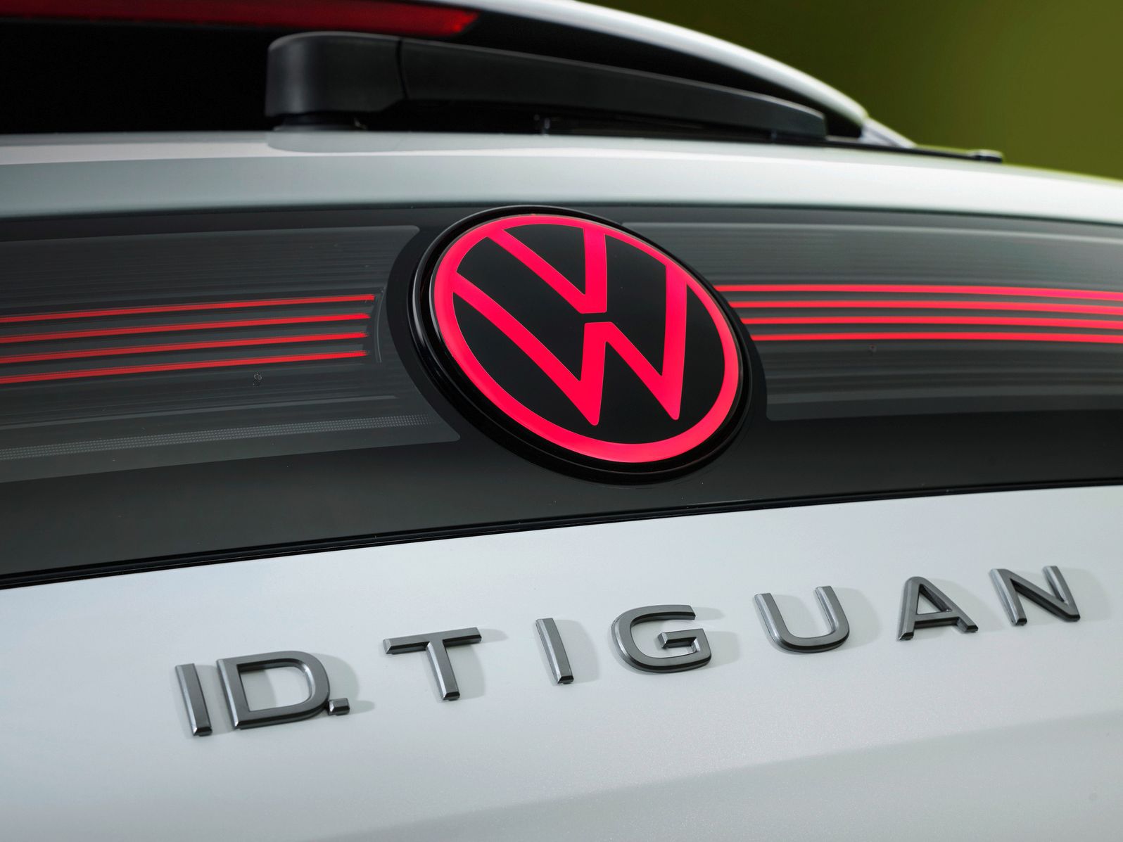 Detailný pohľad na osvetlené logo VW a názov modelu ID. Tiguan na zadných dverách bieleho vozidla.