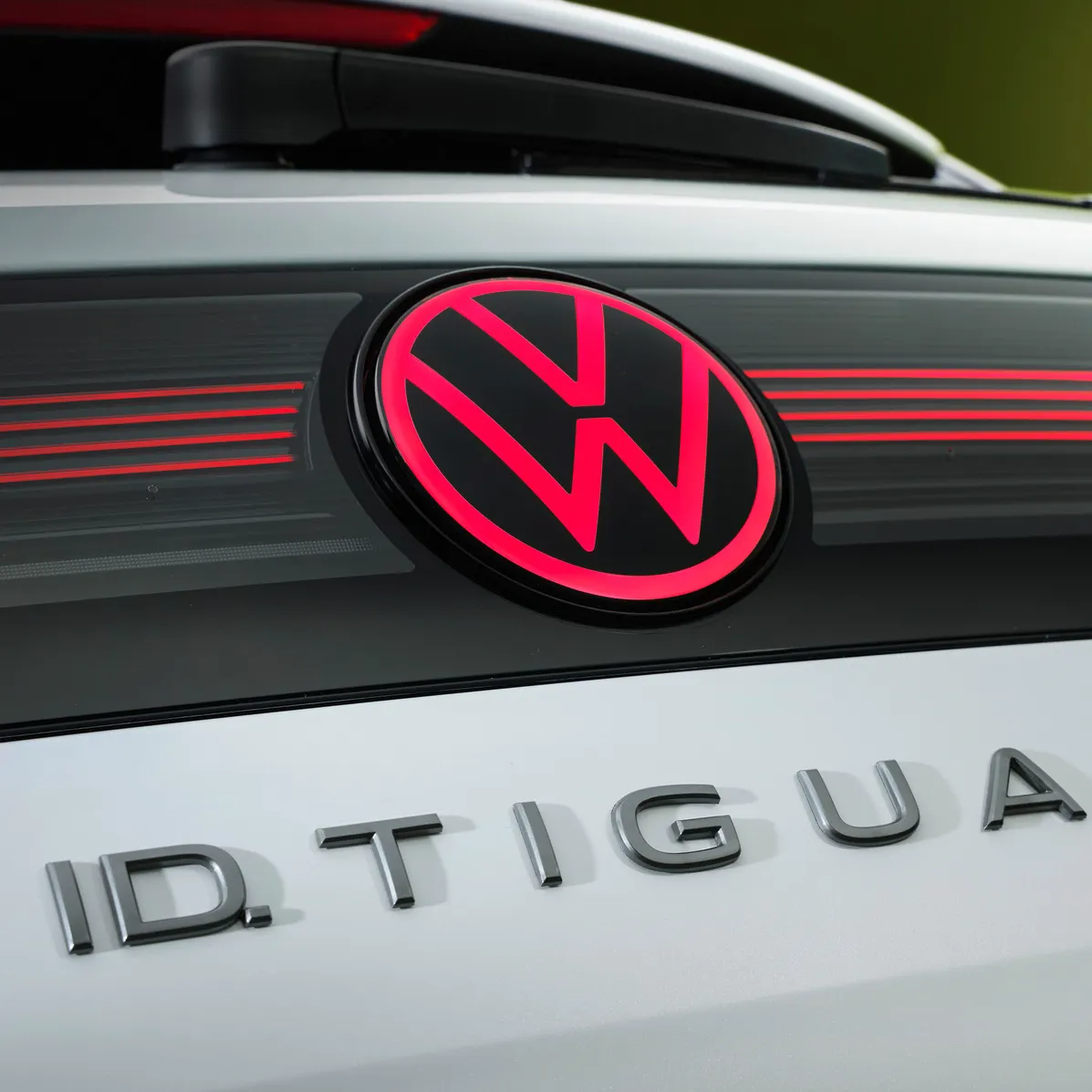 Detailný pohľad na osvetlené logo VW a názov modelu ID. Tiguan na zadných dverách bieleho vozidla.