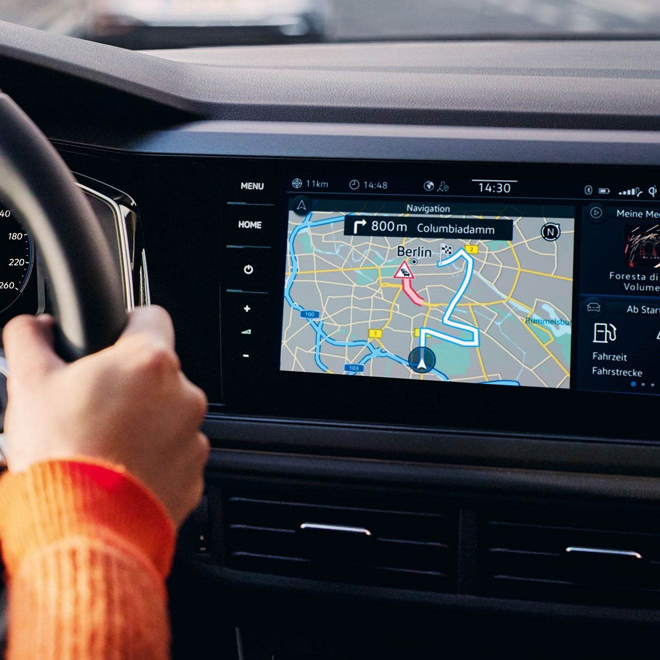 Pohľad do interiéru VW Polo s detailom na displej systému infotainment s ovládacími tlačidlami na bokoch. Na displeji je navigačná mapa. Čiastočne možno vidieť ruku, ktorá drží volant a prístrojový panel.