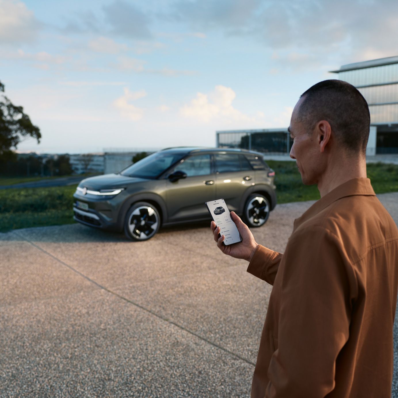 Zelený VW ID.Cross stojí pri obytnom dome, vedľa neho stojí muž, ktorý sa pozerá do svojho smartfónu.
