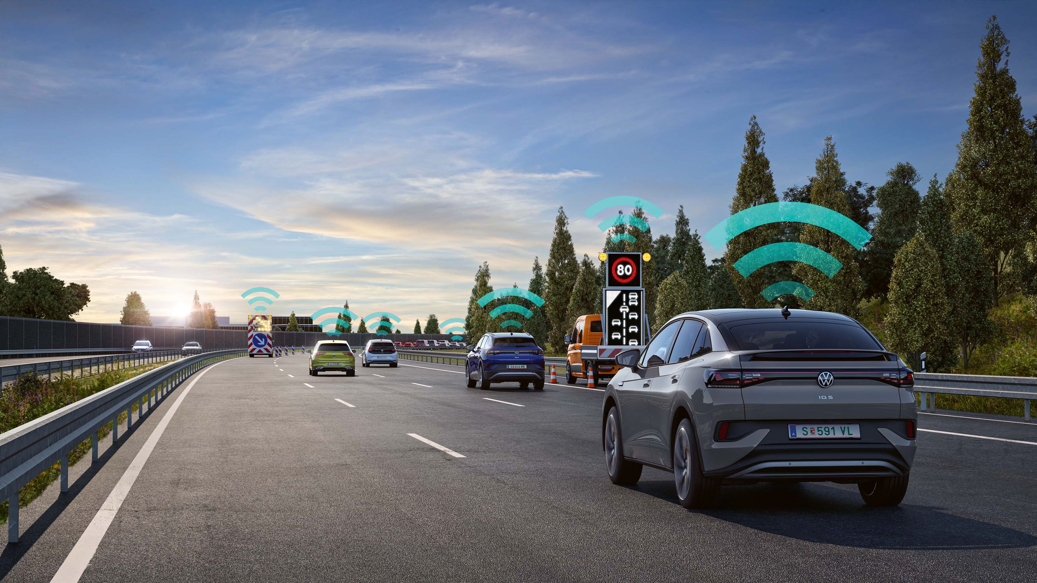 Na obrázku je diaľnica so štyrmi pruhmi a niekoľkými automobilmi.  Nad vozidlami je graficky zobrazená ikona WiFi, ktorá znázorňuje vzájomné prepojenie vozidiel a systém Varovania pred nebezpečenstvom. 