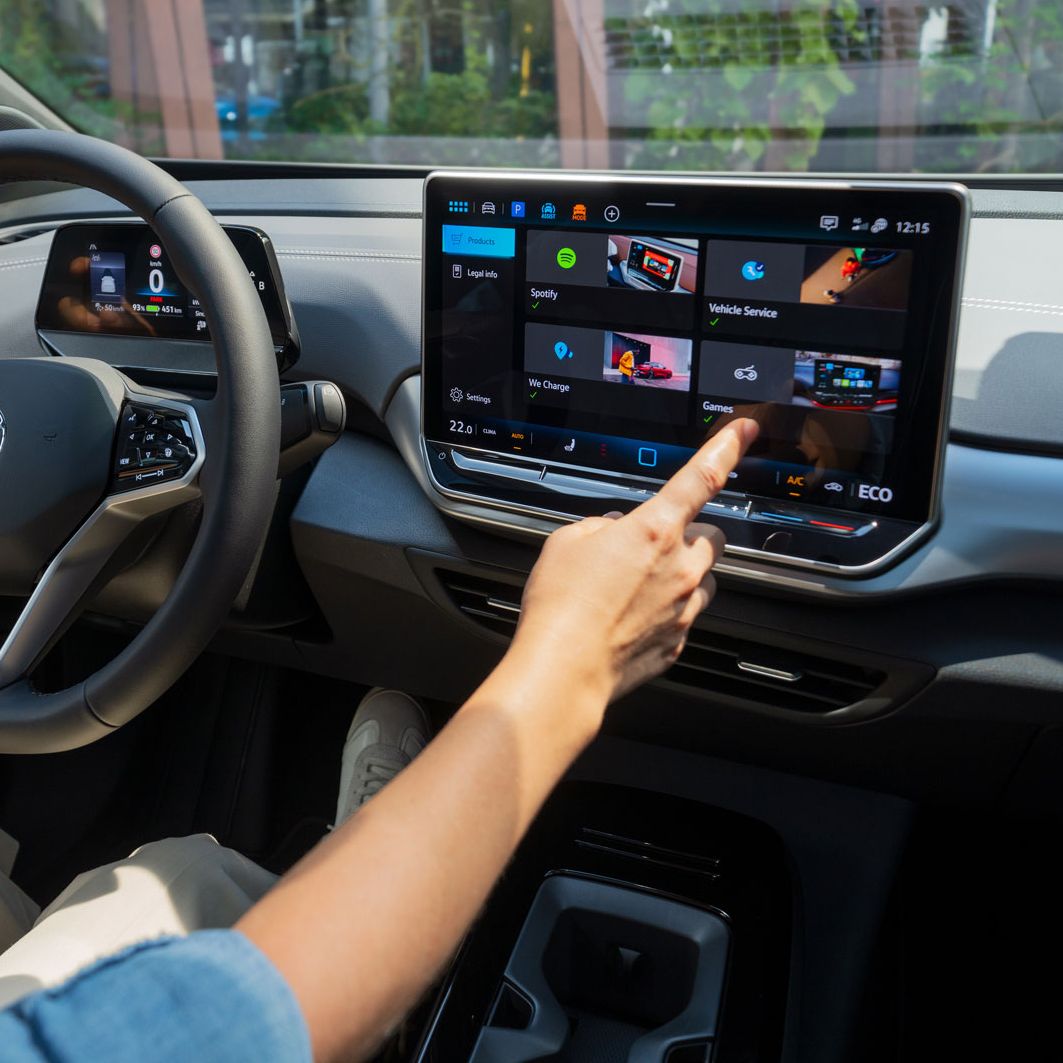 Pohľad na osobu na mieste vodiča, ktorá prstom ukazuje na displej systému inoftainment. Ľavou rukou drží multifunkčný volant.