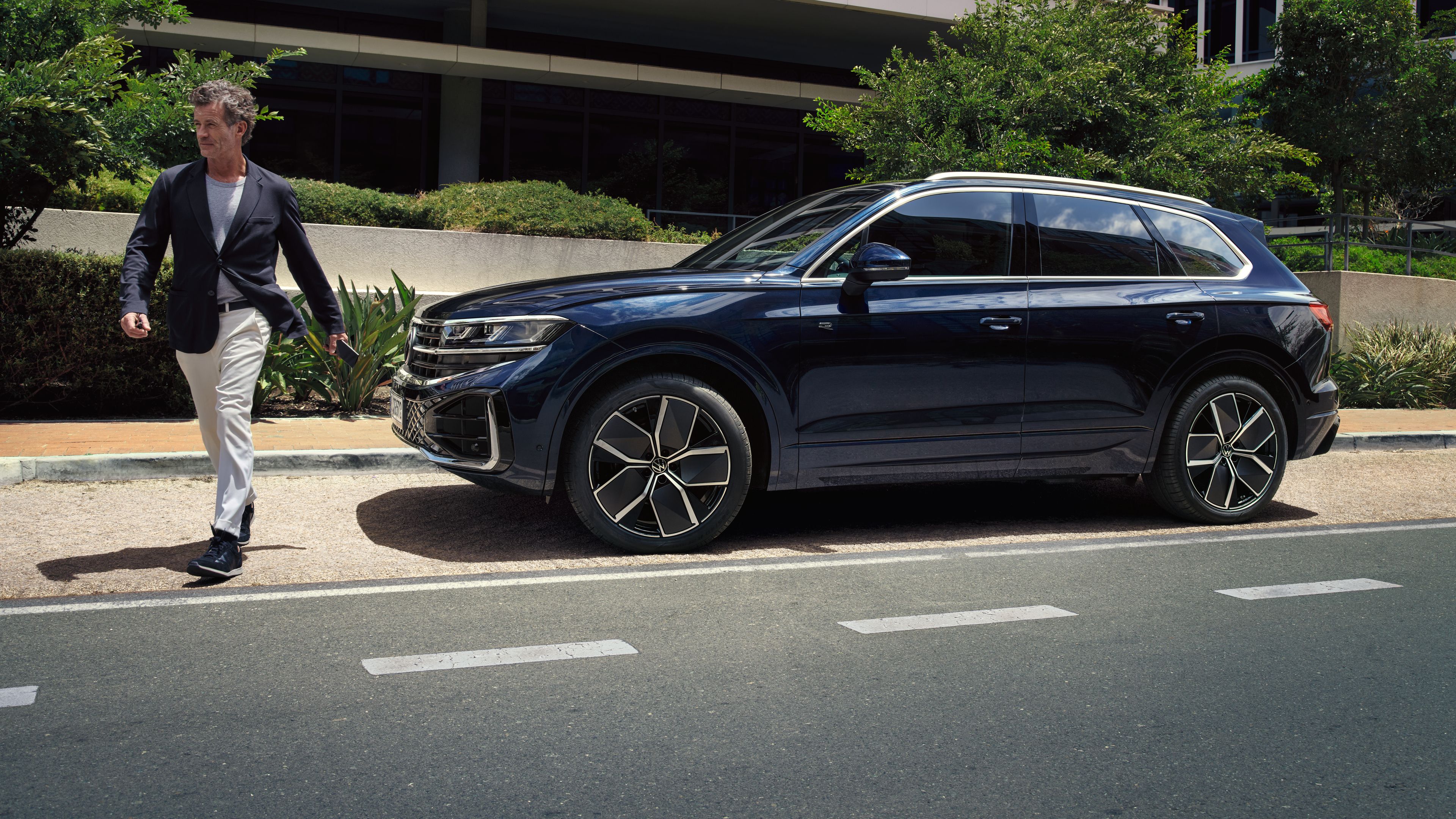 Ein Mann geht an einem parkenden VW Touareg R-Line vorbei.