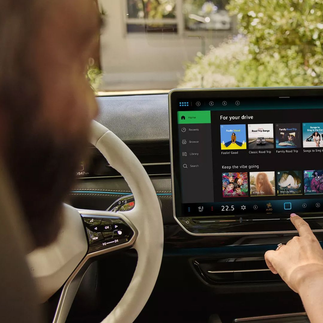 Muž a žena sedia vo vozidle Volkswagen a prostredníctvom displeja na palubnej doske ovládajú službu Spotify. 