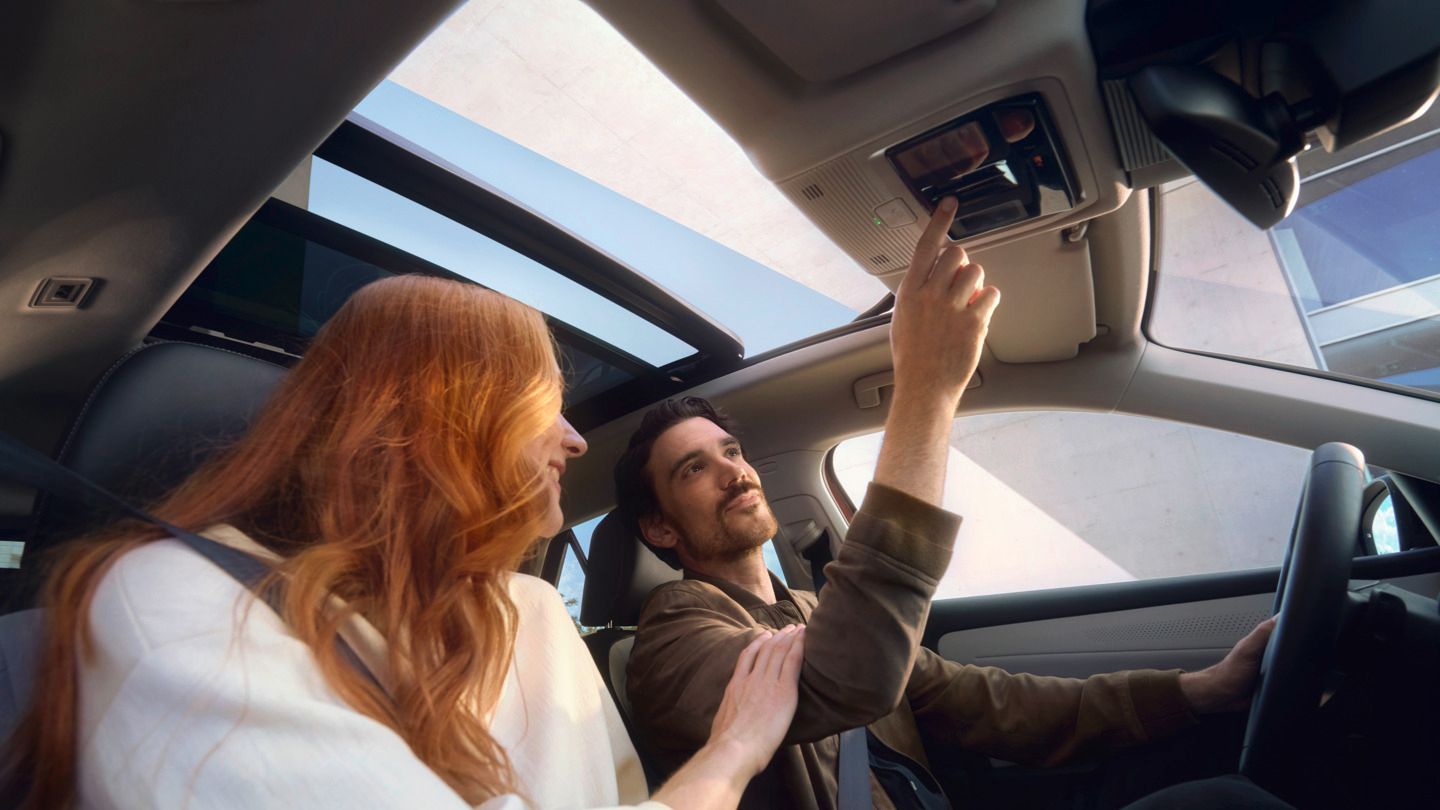 V novom VW T-Roc sedia dve osoby, jedna z nich má červené vlasy a druhá stláča tlačidlo na streche. Auto má panoramatickú strechu.