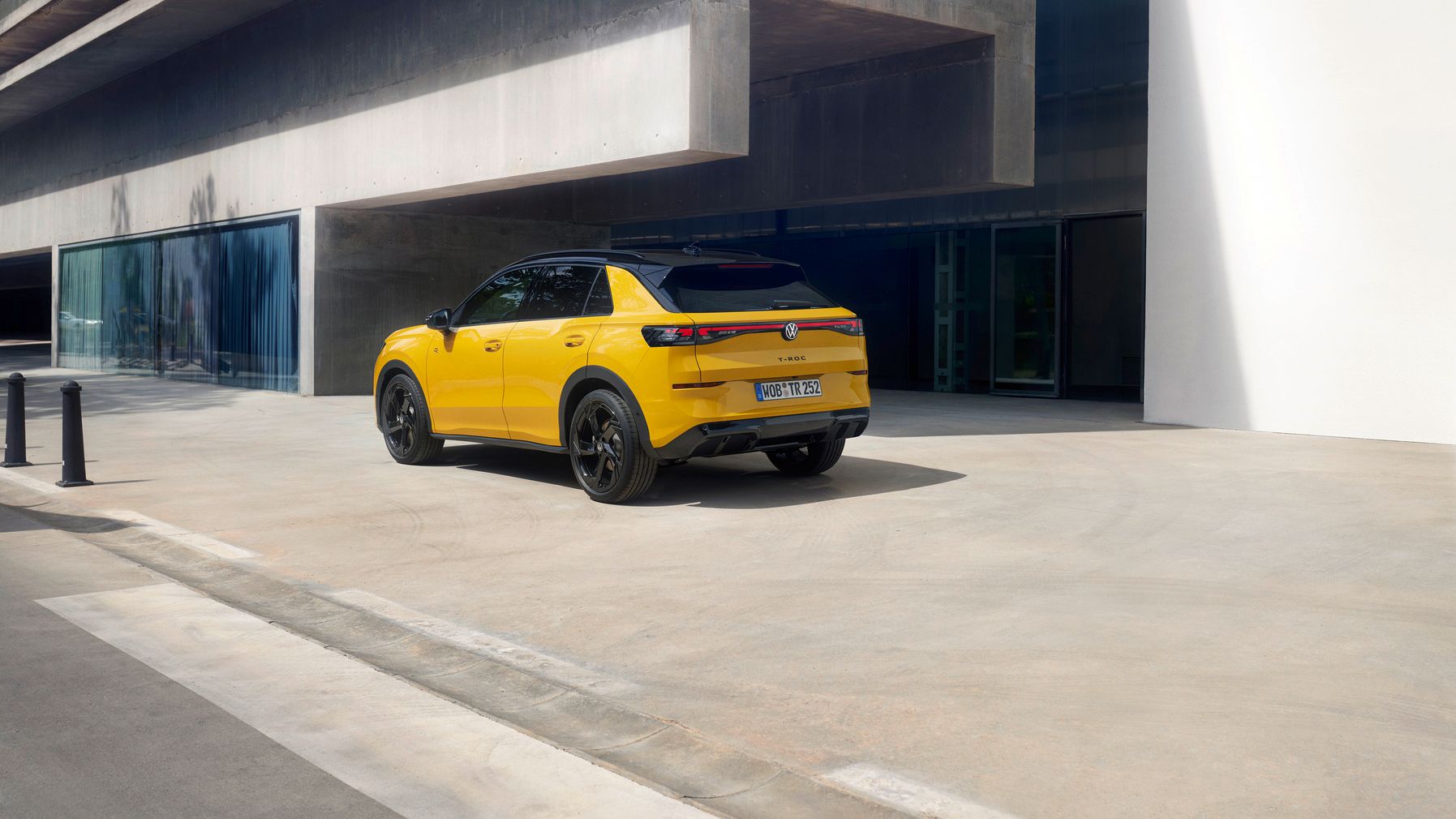 Pohľad na zadné partie Volkswagen T-roc. Vozidlo je zaparkované pre modernou, exkluzívnou betónovou budovou.