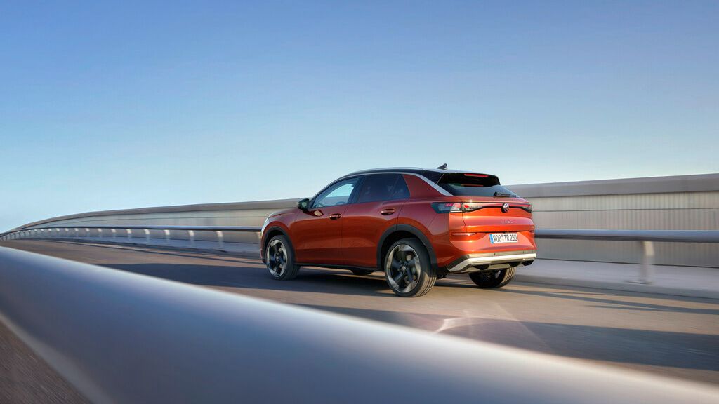 Červený SUV automobil jazdí po modernom moste. Vozidlo má športový dizajn a tmavé zadné okná. Obloha je jasná a modrá.