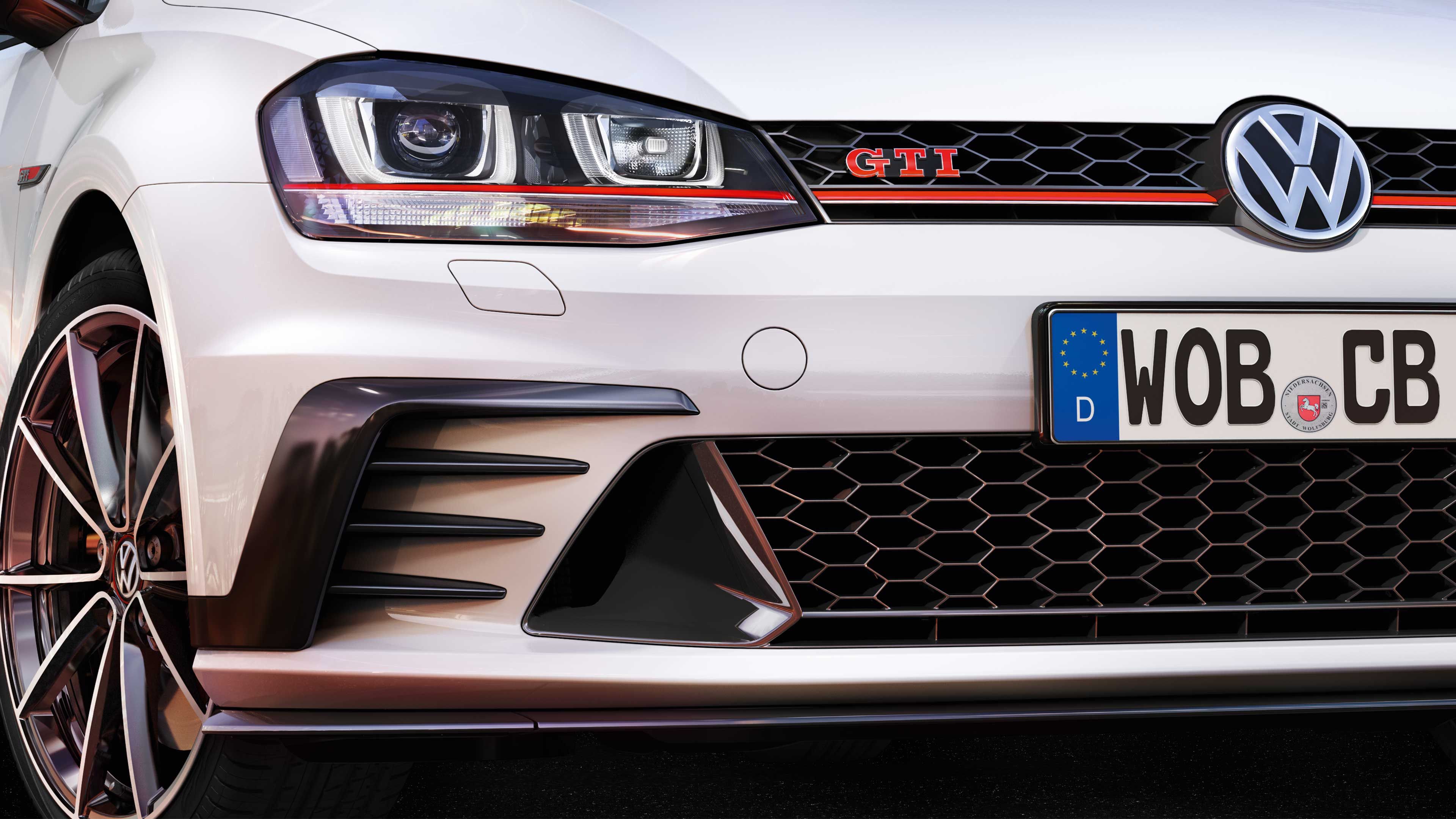 Predná časť bieleho automobilu Golf GTI so znateľným logom VW na kapote. Automobil má nemeckú poznávaciu značku. detail na výrazné svetlomety, športové disky kolies a športový dizajn.