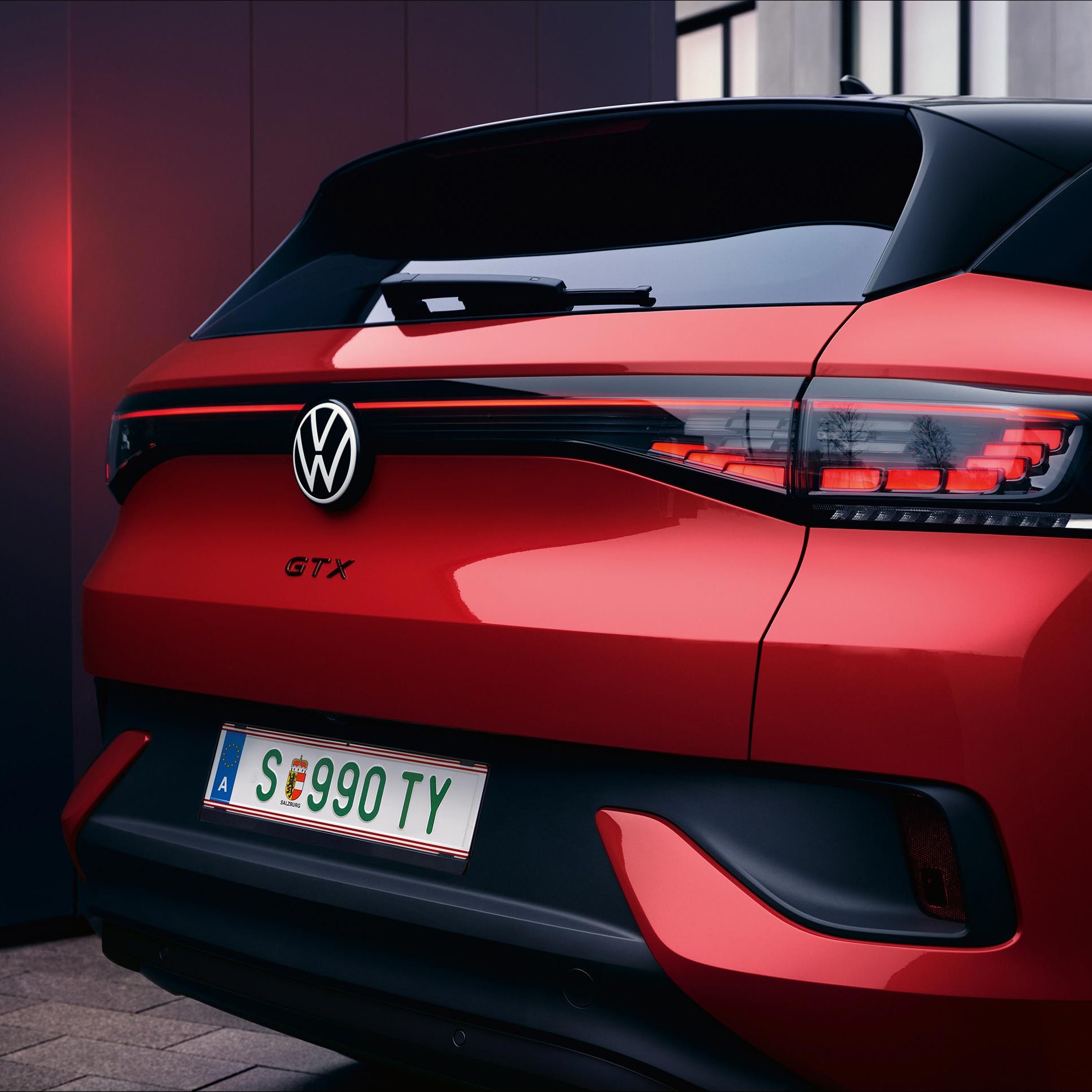 VW ID.4 GTX v červenej farbe. Pohľad na zadné partie vozidla. Zadné svetlá sú zatvorené, svetlo sa odráža v tmavej stene. 
