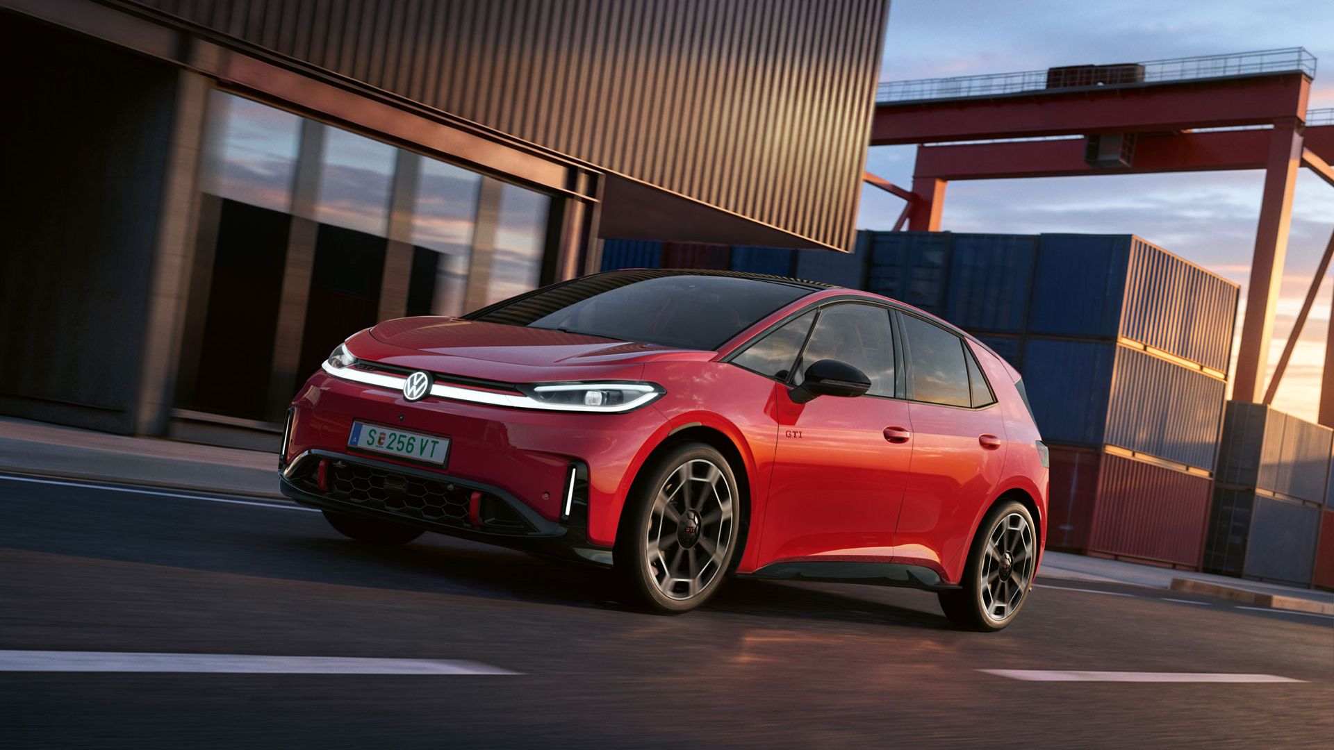 [AI-modified] – Červený VW ID.3 GTI prechádza okolo prístavnej budovy so zapnutými svetlometmi a rozsvieteným logom.