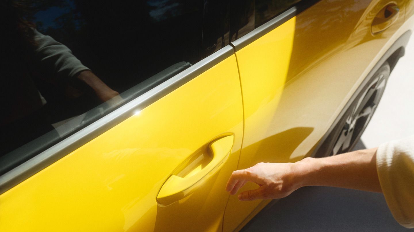 Človek siaha po kľučke dverí žltého auta. Tieň ruky je viditeľný na svetlej podlahe. Auto stojí na mieste.