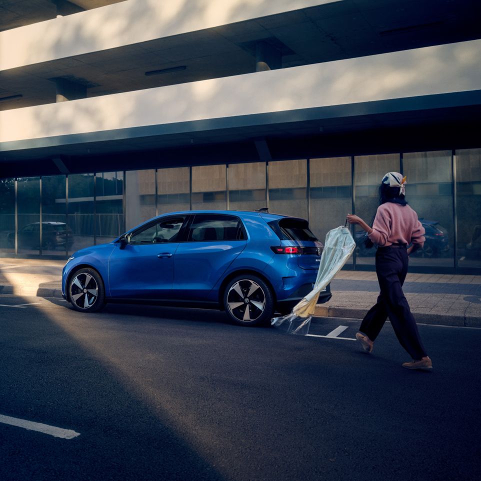 Modrý VW ID. Polo Style stojí zaparkovaný bokom pri okraji cesty, k vozidlu kráča žena.