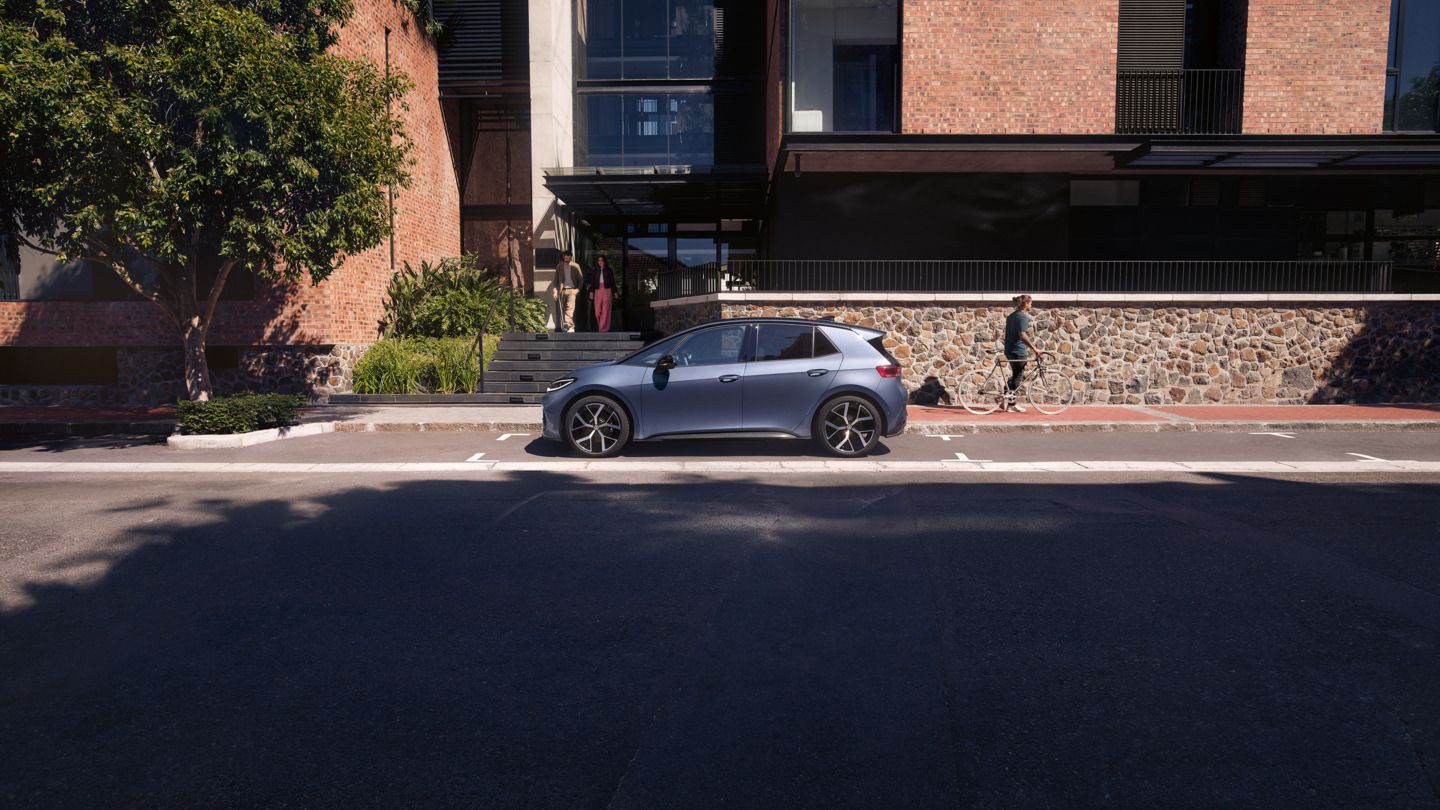 Modrý VW ID.3 Neo parkuje pred obytným domom, z ktorého vychádza žena a muž